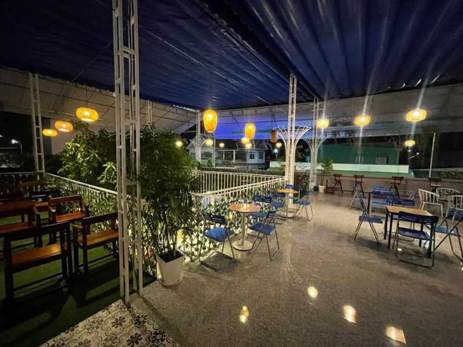 Kh&ocirc;ng gian qu&aacute;n c&agrave; ph&ecirc; ngo&agrave;i trời v&agrave;o ban đ&ecirc;m với b&agrave;n ghế, c&acirc;y xanh v&agrave; đ&egrave;n lồng treo s&aacute;ng.