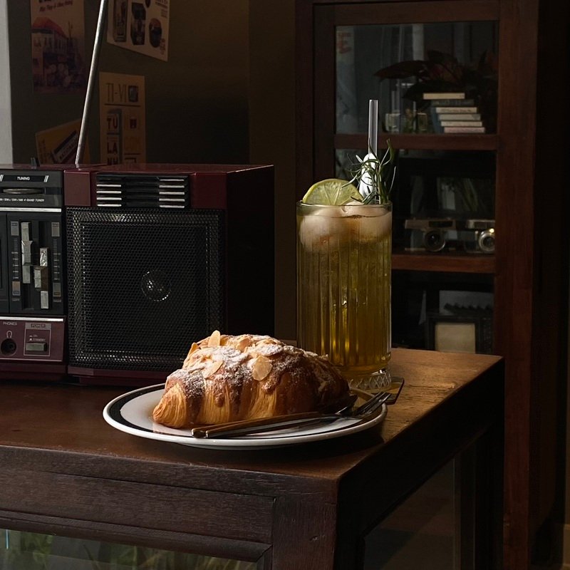 Ly nước c&oacute; đ&aacute; v&agrave; chanh, b&aacute;nh sừng b&ograve; tr&ecirc;n đĩa cạnh radio cổ điển đặt tr&ecirc;n b&agrave;n gỗ.