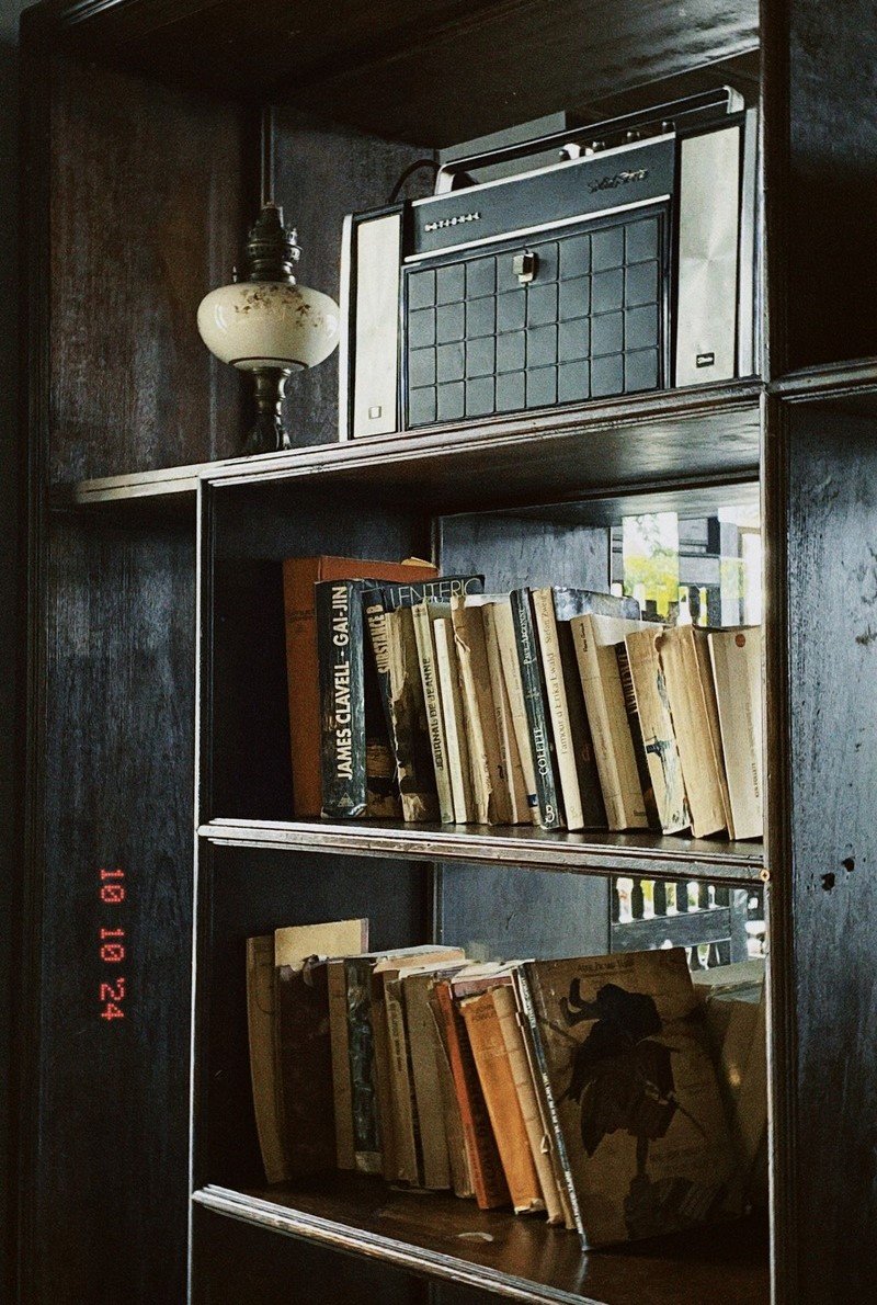 Kệ s&aacute;ch gỗ với nhiều cuốn s&aacute;ch cũ v&agrave; một chiếc đ&agrave;i radio cổ điển b&ecirc;n tr&ecirc;n.