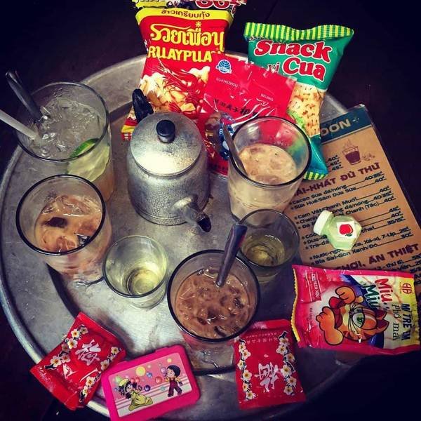 Khung cảnh b&agrave;n với đồ uống, ấm tr&agrave; v&agrave; nhiều loại b&aacute;nh snack đa dạng, c&ugrave;ng thực đơn b&ecirc;n cạnh.