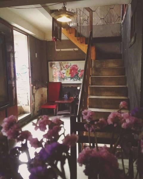 Cầu thang gỗ trong ng&ocirc;i nh&agrave; cũ, b&ecirc;n cạnh l&agrave; b&agrave;n ghế v&agrave; lọ hoa t&iacute;m, &aacute;nh s&aacute;ng từ cửa sổ chiếu v&agrave;o.