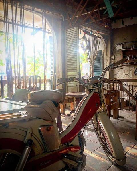 Xe m&aacute;y cổ điển m&agrave;u đỏ trắng đậu trong qu&aacute;n c&agrave; ph&ecirc; với &aacute;nh s&aacute;ng tự nhi&ecirc;n chiếu qua cửa sổ.