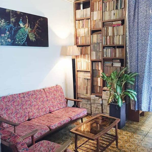 Ph&ograve;ng kh&aacute;ch với ghế hoa, b&agrave;n k&iacute;nh, kệ s&aacute;ch lớn, chậu c&acirc;y xanh v&agrave; tranh tường, tạo kh&ocirc;ng gian ấm c&uacute;ng v&agrave; cổ điển.