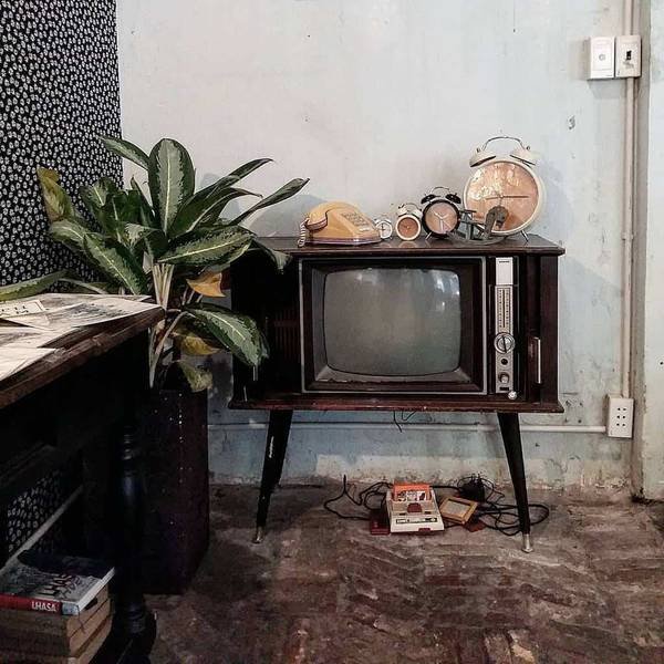 Chiếc TV cổ điển với điện thoại, đồng hồ v&agrave; s&aacute;ch tr&ecirc;n kệ, cạnh một chậu c&acirc;y trong kh&ocirc;ng gian ho&agrave;i cổ.