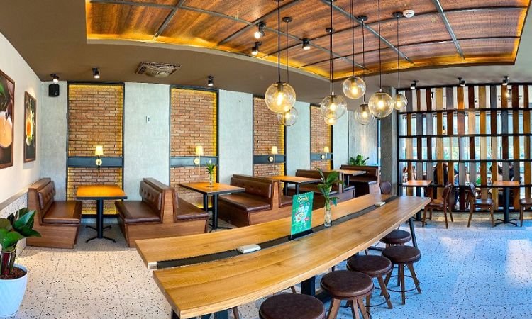 Qu&aacute;n c&agrave; ph&ecirc; hiện đại với b&agrave;n gỗ d&agrave;i, ghế bọc da, đ&egrave;n trần h&igrave;nh cầu v&agrave; tường gạch trang tr&iacute;.