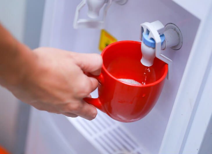 Tay đang r&oacute;t nước v&agrave;o cốc đỏ từ v&ograve;i của m&aacute;y lọc nước.