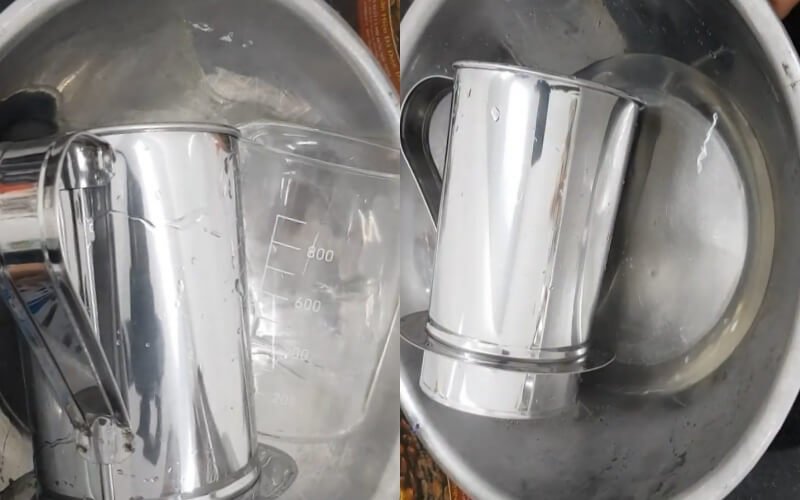 Hai cốc kim loại và một cốc nhựa có vạch chia nằm trong chậu inox, ánh sáng phản chiếu trên bề mặt.