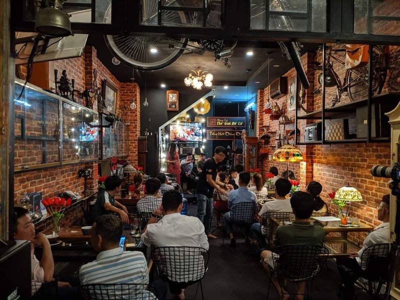 Qu&aacute;n c&agrave; ph&ecirc; ấm c&uacute;ng với tường gạch, &aacute;nh đ&egrave;n v&agrave;ng, nhiều người ngồi tr&ograve; chuyện v&agrave; trang tr&iacute; cổ điển.