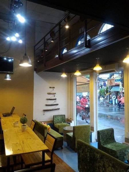 Qu&aacute;n c&agrave; ph&ecirc; nhỏ với b&agrave;n ghế gỗ v&agrave; ghế bọc vải xanh, cửa k&iacute;nh nh&igrave;n ra đường phố nhộn nhịp b&ecirc;n ngo&agrave;i.