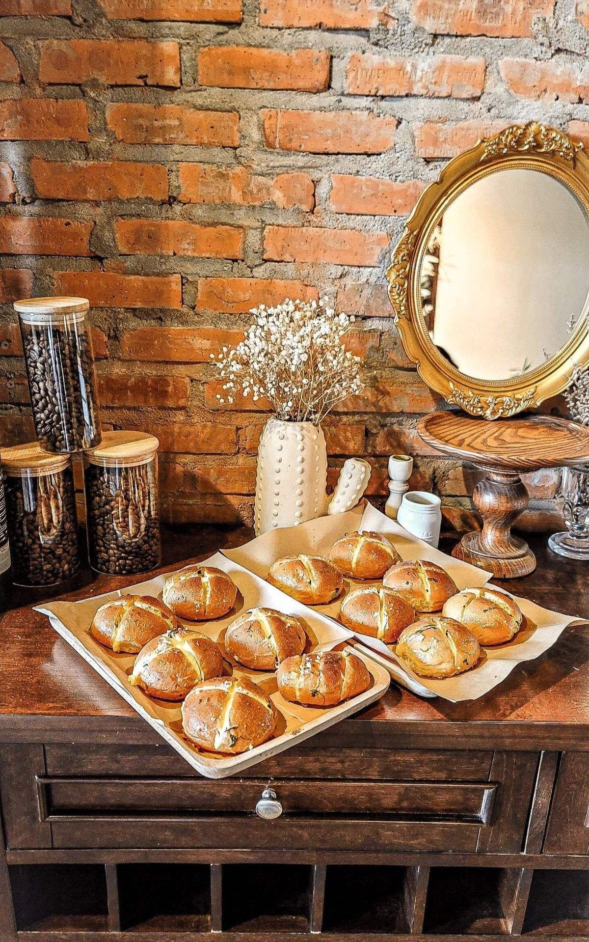 Khay b&aacute;nh mới nướng đặt tr&ecirc;n b&agrave;n gỗ, cạnh lọ hoa kh&ocirc; v&agrave; gương trang tr&iacute;, nền tường gạch.