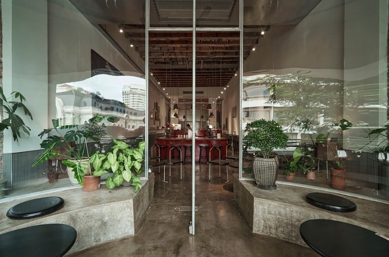 Qu&aacute;n c&agrave; ph&ecirc; với thiết kế hiện đại, cửa k&iacute;nh lớn, c&acirc;y xanh trang tr&iacute;, b&agrave;n ghế sắp xếp ngăn nắp b&ecirc;n trong.