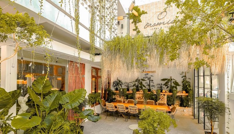 Qu&aacute;n c&agrave; ph&ecirc; ngo&agrave;i trời với b&agrave;n ghế gỗ, c&acirc;y xanh xung quanh, kh&ocirc;ng gian tho&aacute;ng đ&atilde;ng v&agrave; &aacute;nh s&aacute;ng tự nhi&ecirc;n.