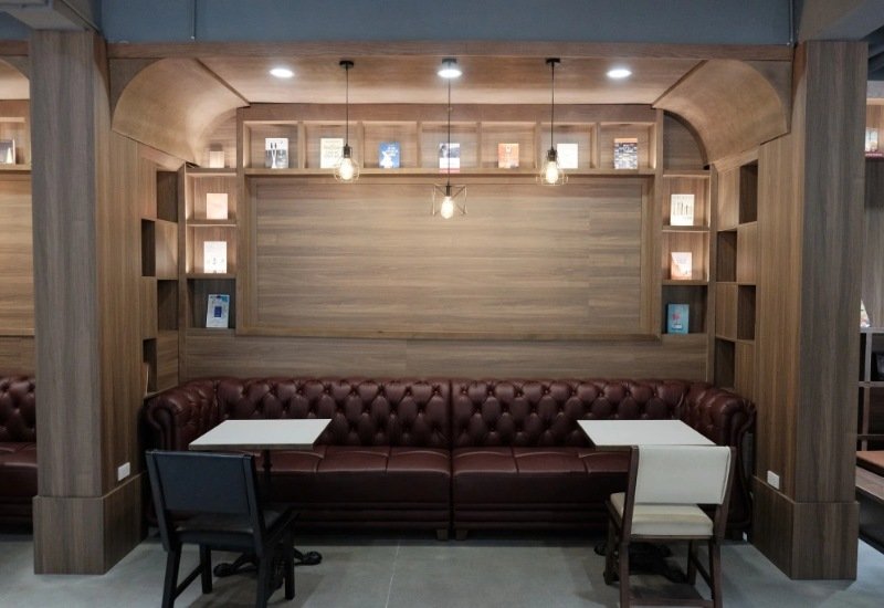 G&oacute;c qu&aacute;n cafe với ghế sofa da, b&agrave;n nhỏ v&agrave; kệ s&aacute;ch trang tr&iacute; tr&ecirc;n tường gỗ, &aacute;nh đ&egrave;n ấm &aacute;p.