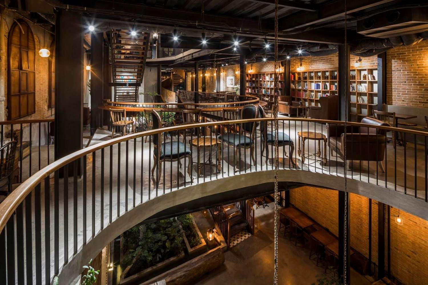 Kh&ocirc;ng gian qu&aacute;n c&agrave; ph&ecirc; hai tầng với nội thất gỗ, &aacute;nh đ&egrave;n ấm &aacute;p v&agrave; kệ s&aacute;ch xếp dọc tường.