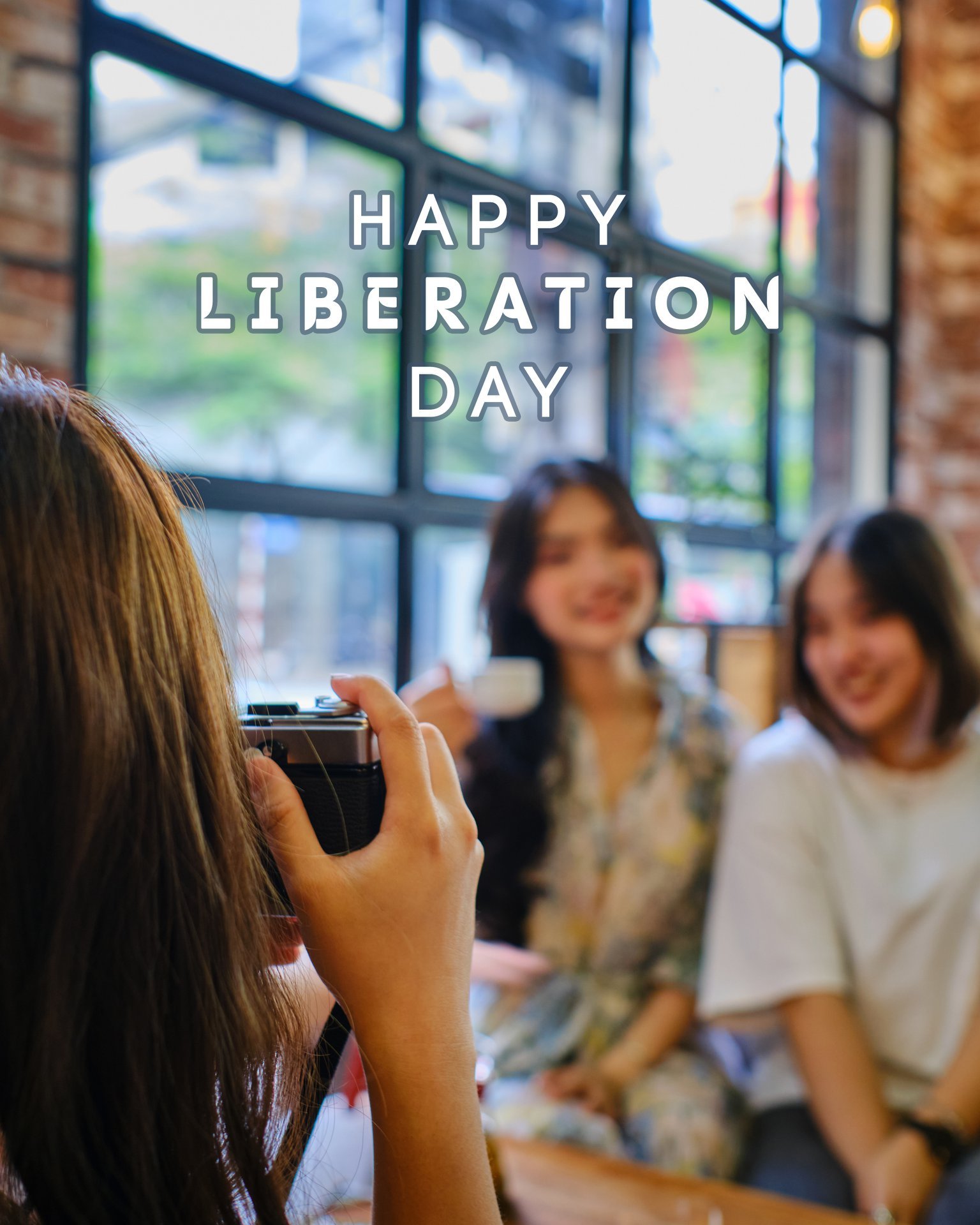 Người cầm m&aacute;y ảnh chụp hai người đang ngồi trong qu&aacute;n c&agrave; ph&ecirc;, d&ograve;ng chữ "Happy Liberation Day" ph&iacute;a tr&ecirc;n.