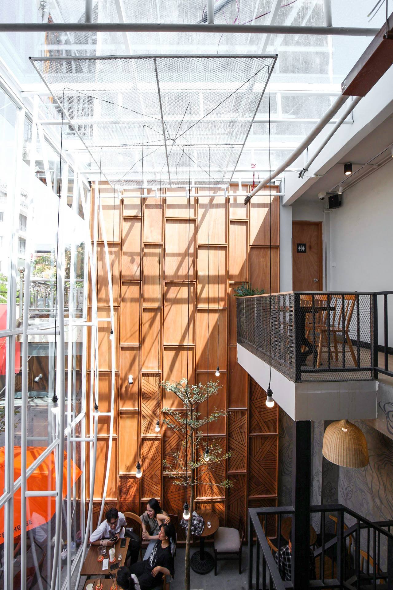 Qu&aacute;n c&agrave; ph&ecirc; với thiết kế mở, &aacute;nh s&aacute;ng tự nhi&ecirc;n, nội thất gỗ, c&acirc;y xanh v&agrave; kh&aacute;ch h&agrave;ng ngồi tr&ograve; chuyện b&ecirc;n b&agrave;n.