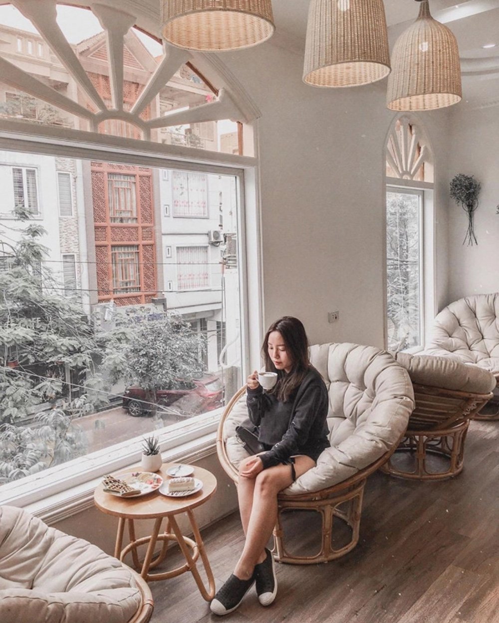 Người ngồi trong qu&aacute;n c&agrave; ph&ecirc;, uống nước, b&ecirc;n cạnh b&agrave;n c&oacute; b&aacute;nh ngọt, cửa sổ lớn nh&igrave;n ra đường phố.