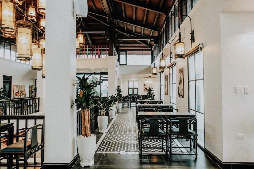 Kh&ocirc;ng gian nội thất với b&agrave;n ghế gỗ, đ&egrave;n treo v&agrave; c&acirc;y xanh trong chậu, thiết kế theo phong c&aacute;ch hiện đại v&agrave; tho&aacute;ng đ&atilde;ng.