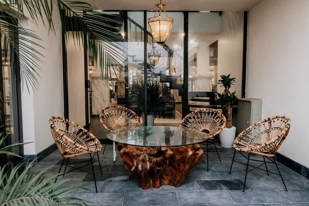 B&agrave;n k&iacute;nh v&agrave; ghế m&acirc;y đặt trong kh&ocirc;ng gian nội thất hiện đại, xung quanh l&agrave; c&acirc;y xanh v&agrave; đ&egrave;n treo trang tr&iacute;.