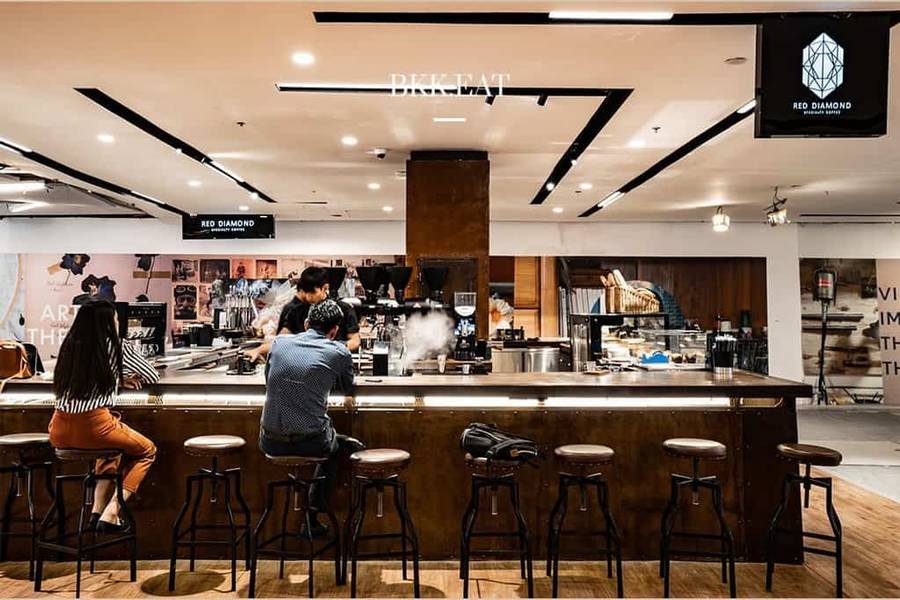 Qu&aacute;n c&agrave; ph&ecirc; hiện đại với quầy bar trung t&acirc;m, c&oacute; kh&aacute;ch h&agrave;ng đang ngồi thưởng thức đồ uống.