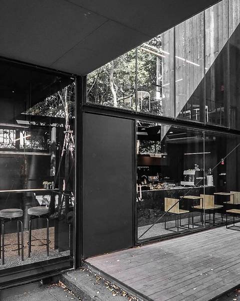 Qu&aacute;n c&agrave; ph&ecirc; c&oacute; thiết kế hiện đại với cửa k&iacute;nh lớn, nội thất tối giản, ghế cao v&agrave; b&agrave;n gỗ.