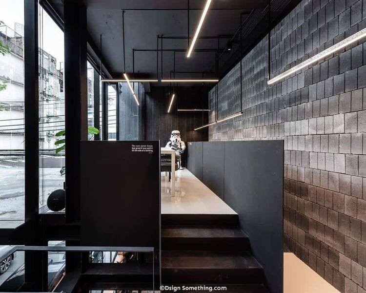 Nội thất qu&aacute;n c&agrave; ph&ecirc; hiện đại với tường b&ecirc; t&ocirc;ng, &aacute;nh s&aacute;ng LED, v&agrave; m&ocirc; h&igrave;nh nh&acirc;n vật trong trang phục trắng ngồi tại b&agrave;n.