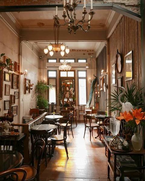 Qu&aacute;n c&agrave; ph&ecirc; phong c&aacute;ch cổ điển, nội thất gỗ v&agrave; trang tr&iacute; c&acirc;y xanh, đ&egrave;n ch&ugrave;m treo trần v&agrave; tranh treo tường.