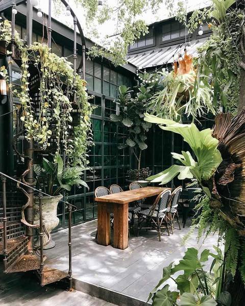 Khu vườn xanh tươi với b&agrave;n gỗ d&agrave;i v&agrave; ghế xung quanh, c&acirc;y cối xum xu&ecirc; v&agrave; &aacute;nh s&aacute;ng tự nhi&ecirc;n từ cửa sổ lớn.