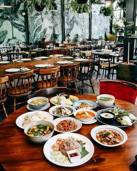 B&agrave;n ăn trong nh&agrave; h&agrave;ng trang tr&iacute; c&acirc;y xanh, b&agrave;y biện nhiều m&oacute;n ăn đa dạng tr&ecirc;n đĩa trắng v&agrave; t&ocirc; sứ.