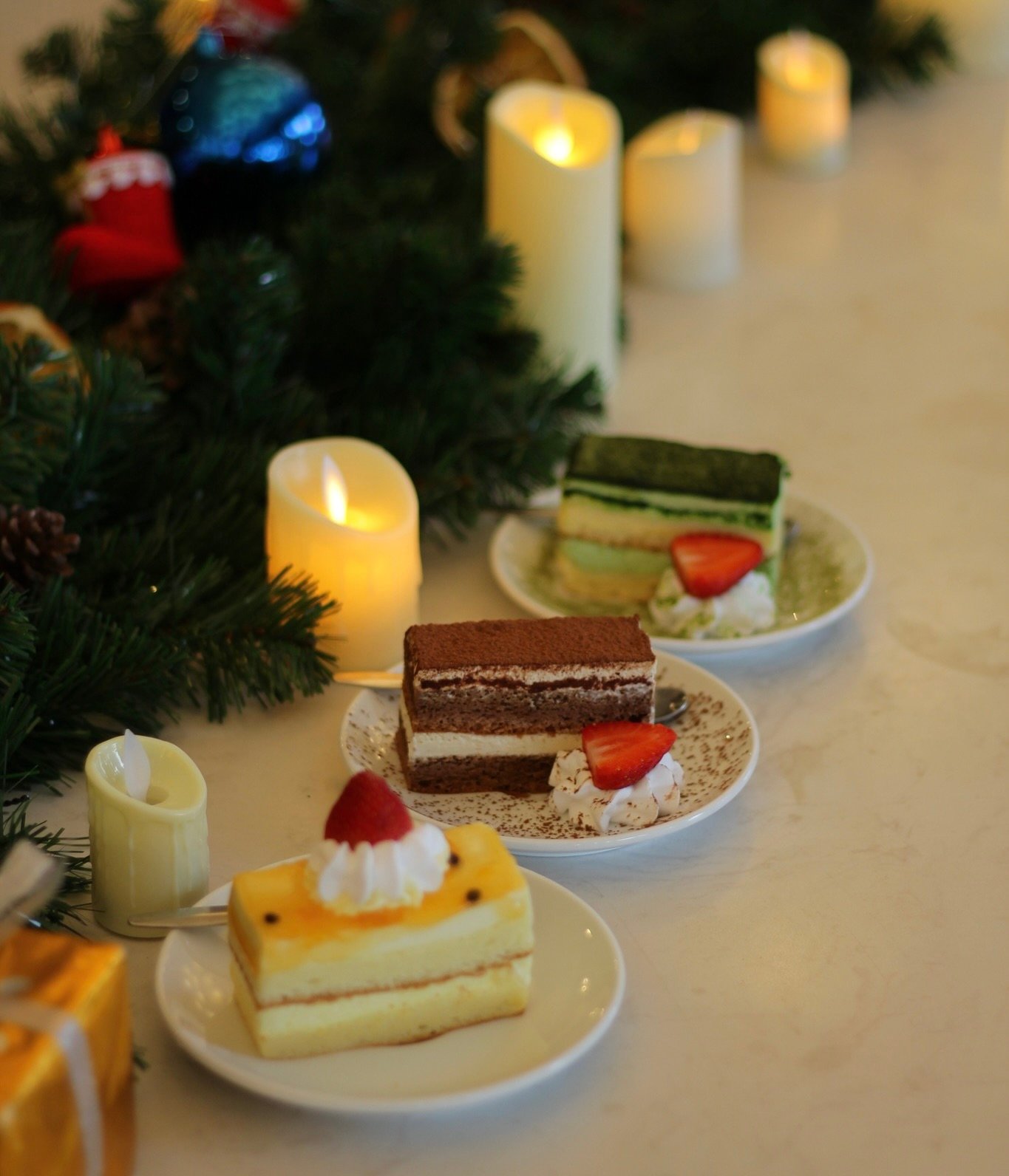 Những chiếc b&aacute;nh ngọt tr&ecirc;n đĩa trắng, trang tr&iacute; d&acirc;u t&acirc;y, nằm tr&ecirc;n b&agrave;n cạnh nến v&agrave; v&ograve;ng hoa xanh.