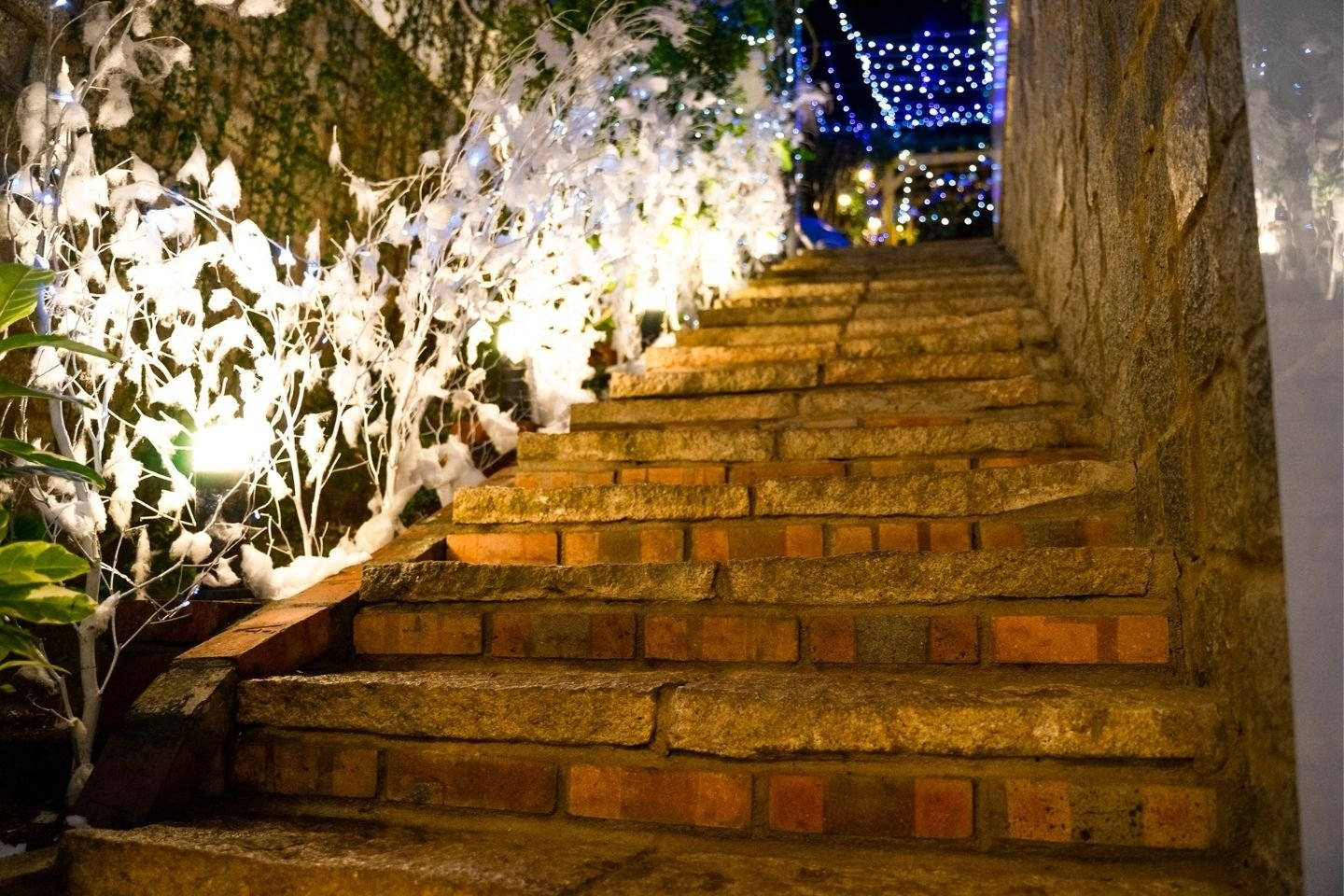 Cầu thang đ&aacute; l&ecirc;n cao, trang tr&iacute; với đ&egrave;n LED v&agrave; c&acirc;y phủ tuyết giả, tạo kh&ocirc;ng kh&iacute; lễ hội ban đ&ecirc;m.