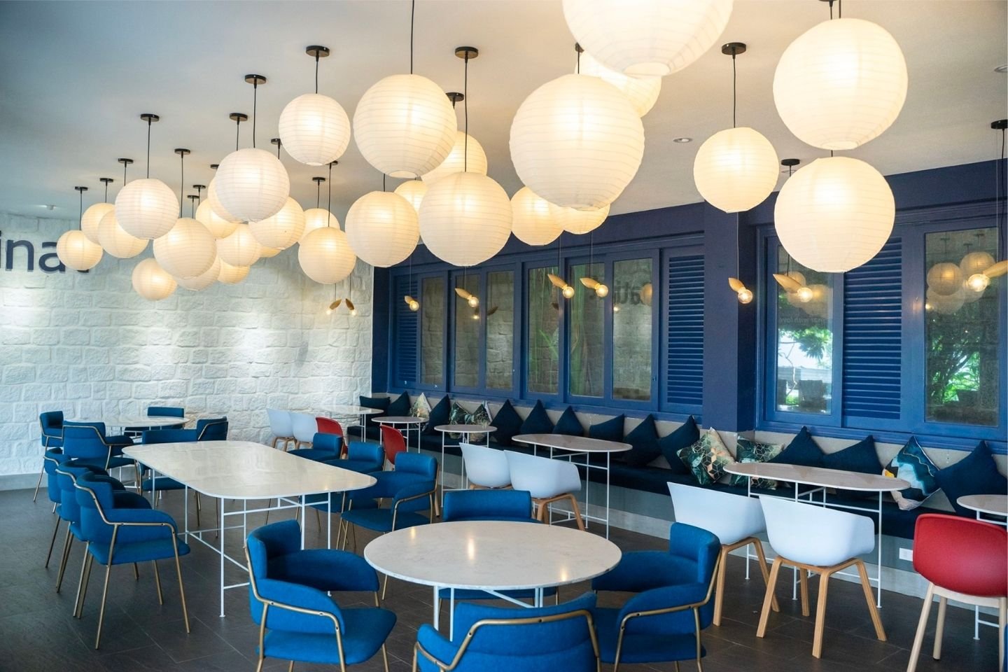 Qu&aacute;n c&agrave; ph&ecirc; với b&agrave;n ghế m&agrave;u xanh dương v&agrave; trắng, đ&egrave;n lồng giấy trắng treo trần, tường m&agrave;u xanh v&agrave; trắng.