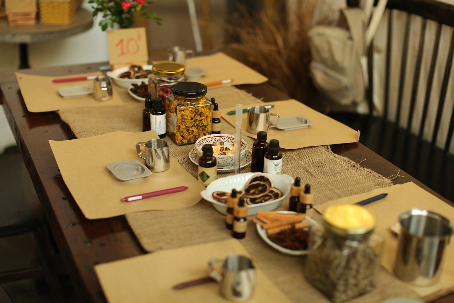 B&agrave;n gỗ được sắp xếp với c&aacute;c lọ thủy tinh, chai lọ, b&uacute;t viết v&agrave; c&aacute;c đĩa chứa nguy&ecirc;n liệu tự nhi&ecirc;n.