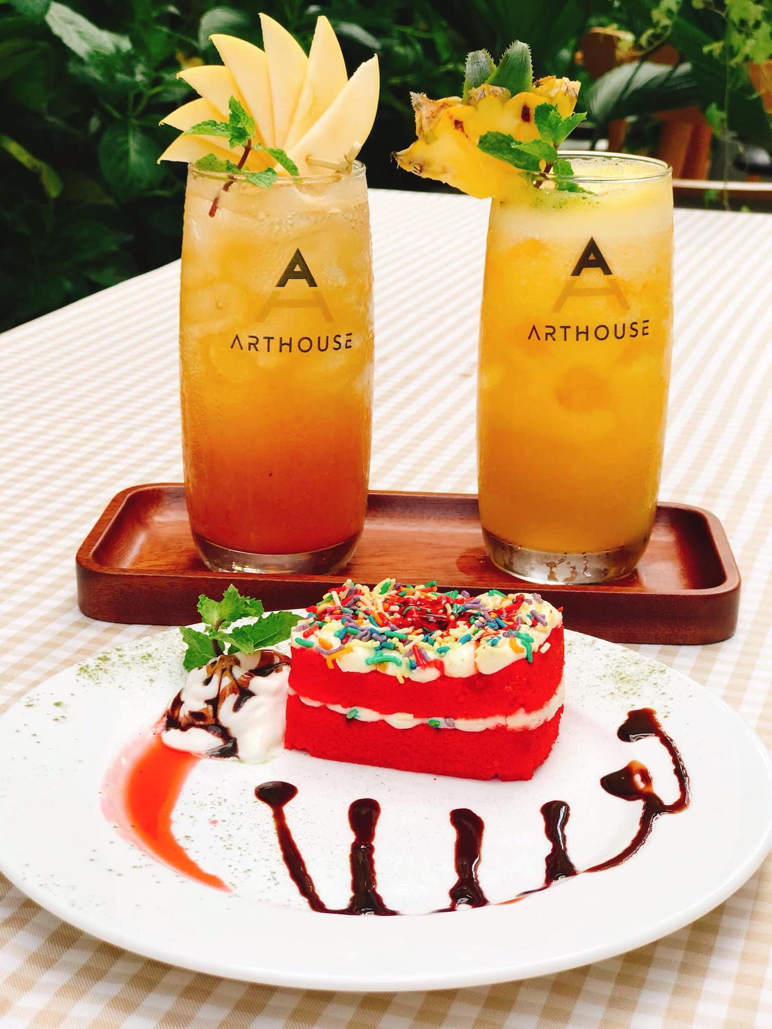 Hai ly nước trái cây trang trí trái cây và bánh kem đỏ với kem phủ màu sắc trên bàn kẻ sọc.