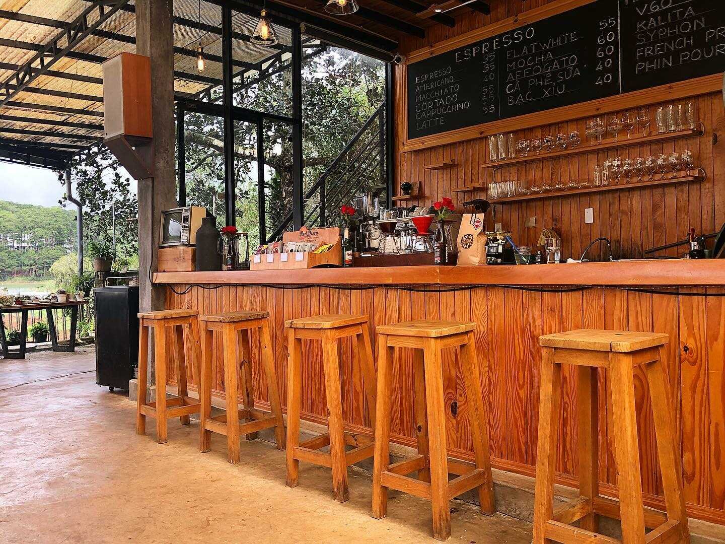 Qu&aacute;n c&agrave; ph&ecirc; với quầy gỗ, ghế ngồi, bảng menu tr&ecirc;n tường, kh&ocirc;ng gian mở ra khung cảnh thi&ecirc;n nhi&ecirc;n.