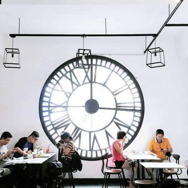 Một nhóm người ngồi ăn uống bên dưới chiếc đồng hồ lớn trên tường trong một quán cà phê.