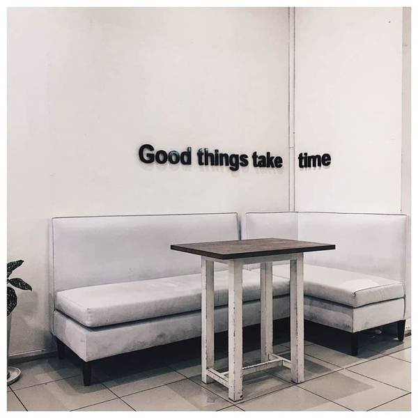 Góc phòng với ghế sofa trắng chữ L, bàn gỗ nhỏ và dòng chữ "Good things take time" trên tường.