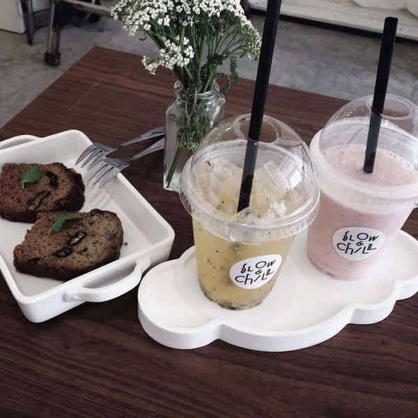 Hai ly nước và hai lát bánh trên bàn gỗ, bên cạnh là bình hoa nhỏ.