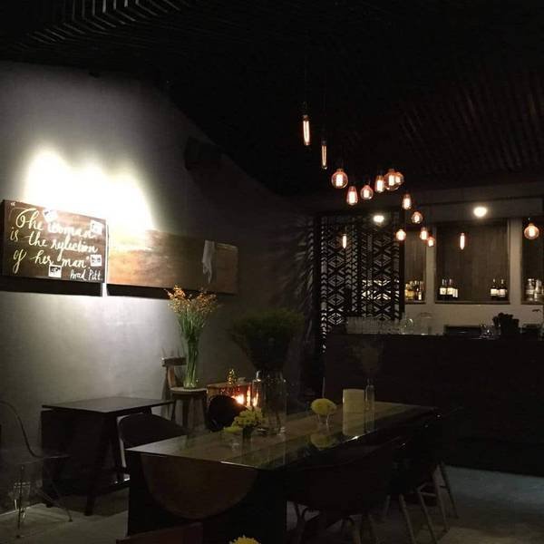 Không gian quán cà phê ấm cúng với ánh đèn vàng, bàn ghế gỗ và trang trí hoa tươi, tạo cảm giác thư giãn.