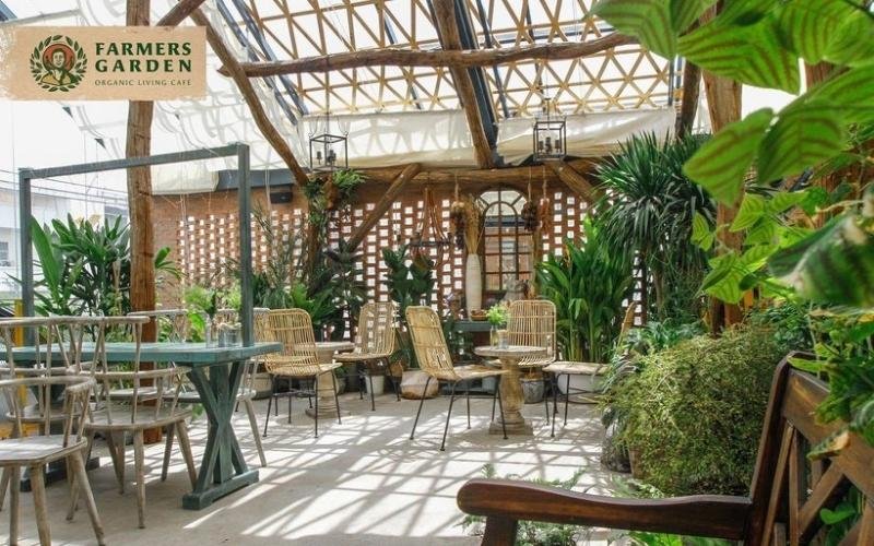 Quán cà phê với không gian mở, bàn ghế mây, nhiều cây xanh, ánh sáng tự nhiên, tạo cảm giác thư giãn và gần gũi.