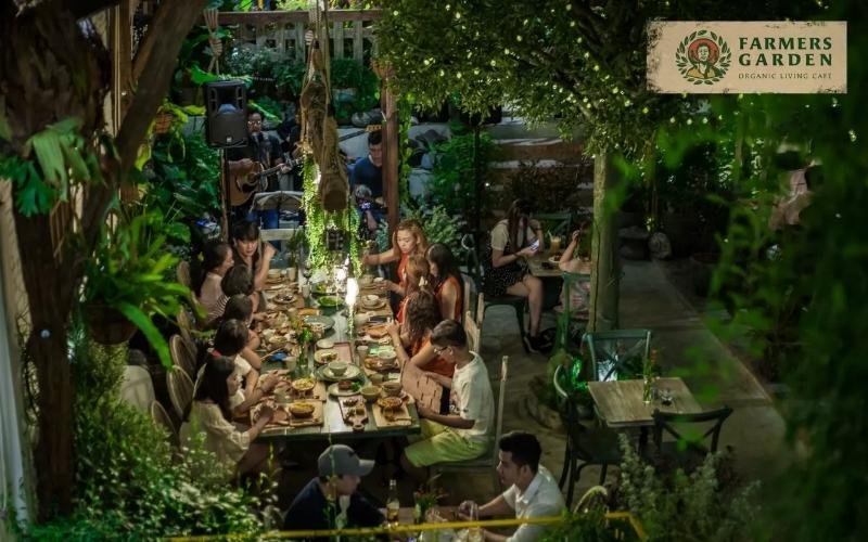 Nhóm người đang ăn tối trong không gian vườn xanh mát, dưới ánh đèn vàng, tạo cảm giác ấm cúng và thư giãn.