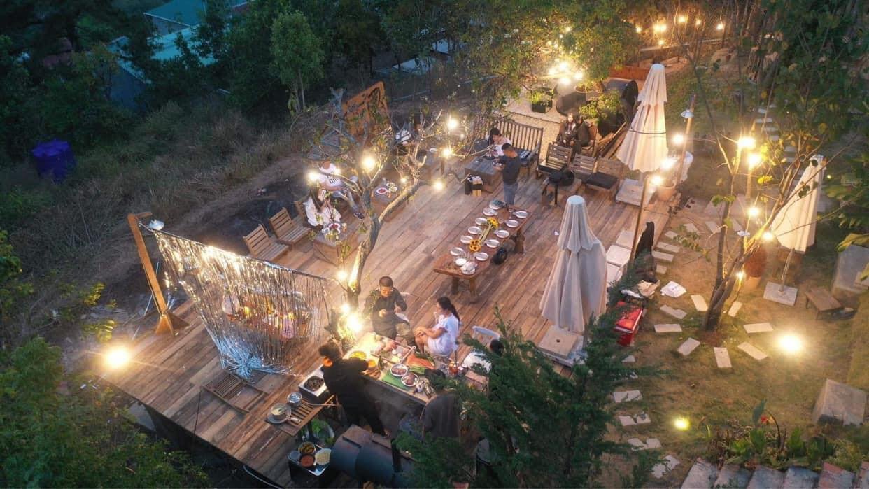 Bữa tiệc ngo&agrave;i trời buổi tối với &aacute;nh đ&egrave;n lung linh, b&agrave;n ăn lớn v&agrave; nhiều người tham dự tr&ecirc;n s&acirc;n gỗ.