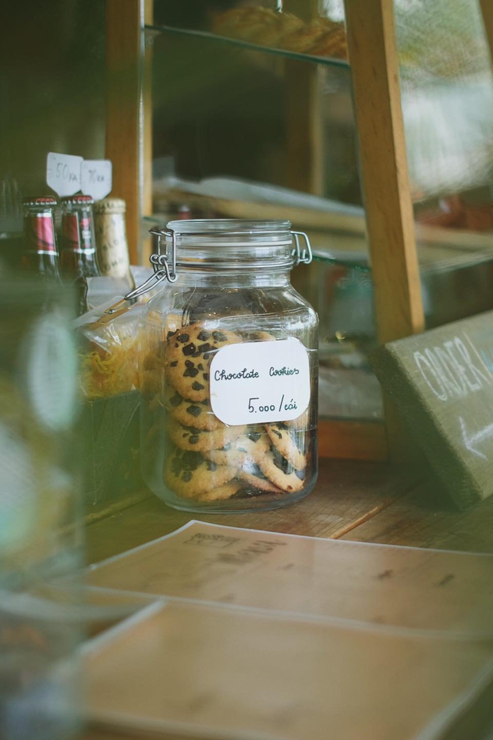 Hũ thủy tinh chứa b&aacute;nh quy s&ocirc; c&ocirc; la, c&oacute; gi&aacute; 5.000 đồng mỗi c&aacute;i, đặt tr&ecirc;n kệ gỗ trong cửa h&agrave;ng.
