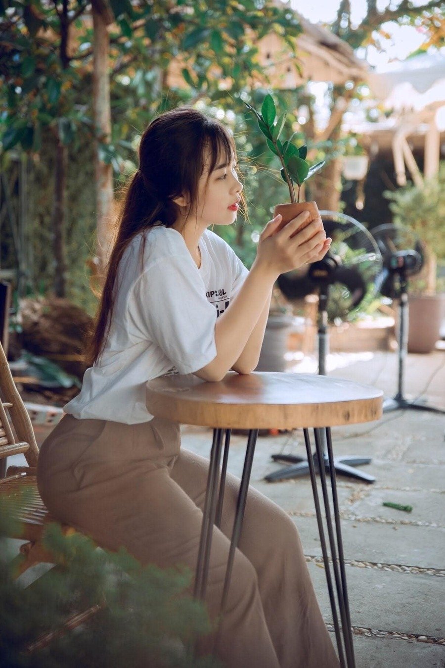 Người phụ nữ ngồi ngo&agrave;i trời, cầm chậu c&acirc;y nhỏ tr&ecirc;n tay, ngắm nh&igrave;n với vẻ suy tư.