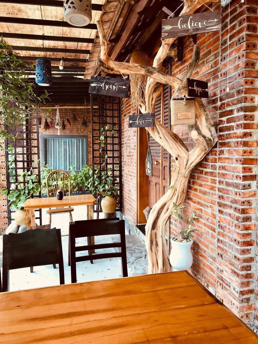 Qu&aacute;n c&agrave; ph&ecirc; với b&agrave;n ghế gỗ, c&acirc;y xanh treo biển chữ, tường gạch đỏ, kh&ocirc;ng gian ấm c&uacute;ng v&agrave; trang tr&iacute; đơn giản.