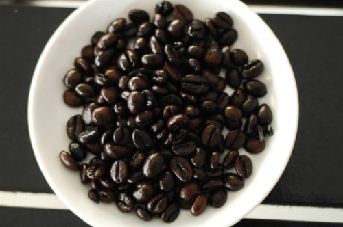 hko-0025-jpg-5341-1435799050 Đĩa chứa đầy hạt cà phê rang sẫm màu, đặt trên bề mặt tối màu.