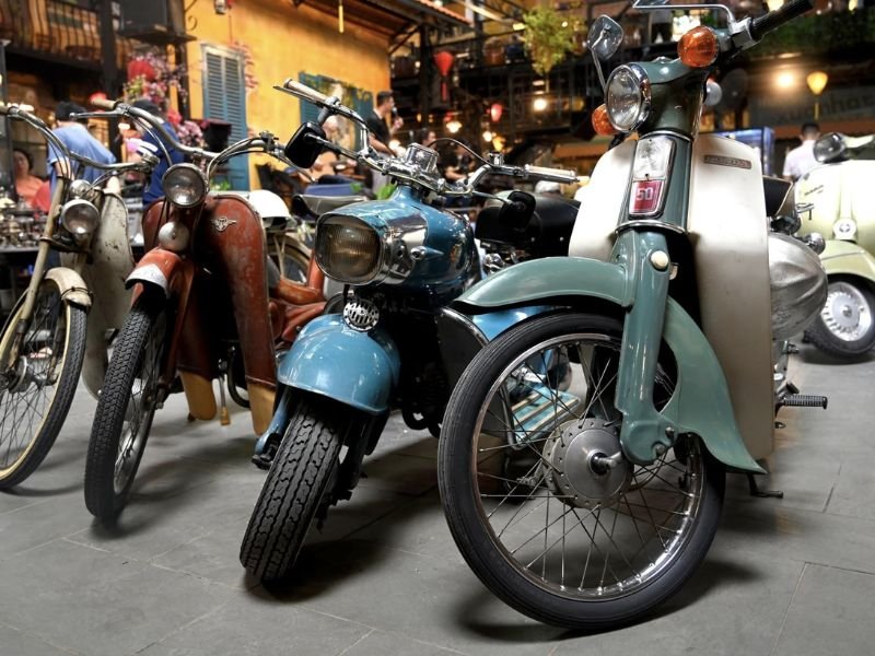 C&aacute;c xe m&aacute;y cổ điển được trưng b&agrave;y trong một kh&ocirc;ng gian qu&aacute;n c&agrave; ph&ecirc; c&oacute; &aacute;nh s&aacute;ng ấm &aacute;p v&agrave; bối cảnh n&aacute;o nhiệt.