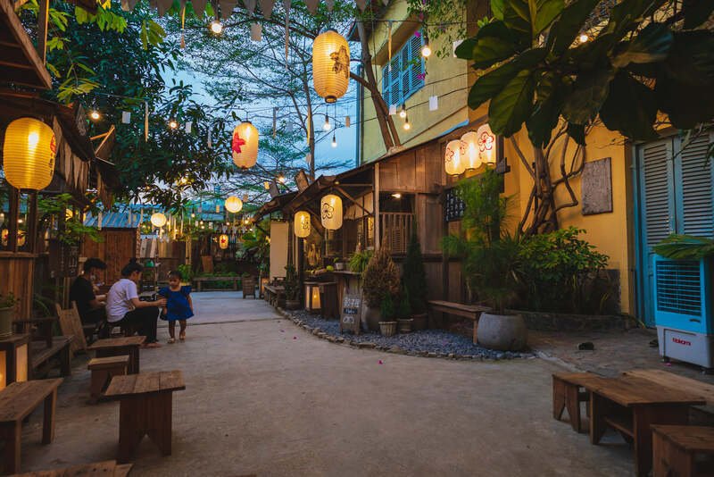 Qu&aacute;n c&agrave; ph&ecirc; phong c&aacute;ch Nhật Bản với đ&egrave;n lồng treo, c&acirc;y xanh xung quanh v&agrave; v&agrave;i người ngồi tr&ograve; chuyện.