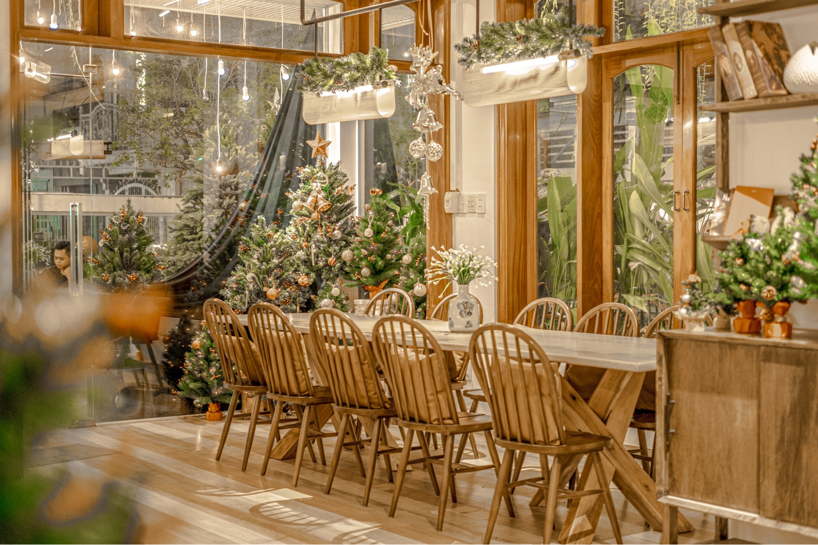 Phòng ăn trang trí Giáng sinh ấm cúng với bàn dài, cây thông Noel và đèn trang trí lấp lánh.