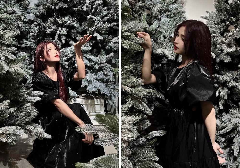 Người phụ nữ mặc váy đen đứng giữa rừng cây thông phủ tuyết, giơ tay cảm nhận không gian xung quanh.